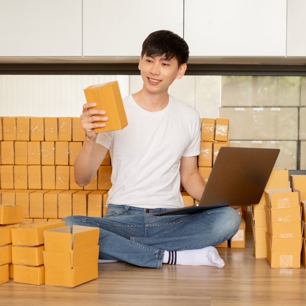 A man surrounded by shipping boxes with a laptop in front