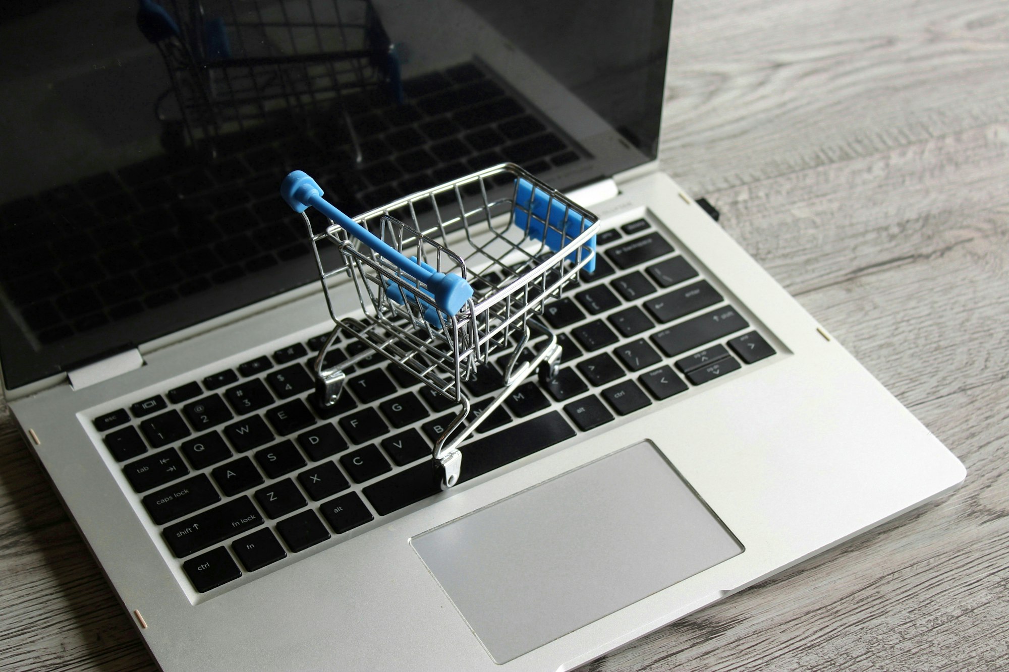 Laptop and mini shopping trolley on wooden table.